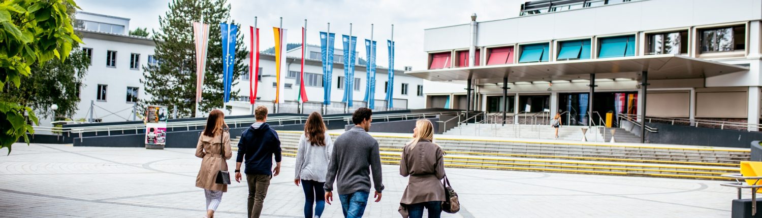 Studierende gehen über den Campus zum Haupteingang der Universität Klagenfurt
