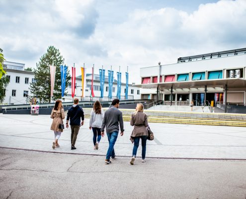 Studierende gehen über den Campus zum Haupteingang der Universität Klagenfurt
