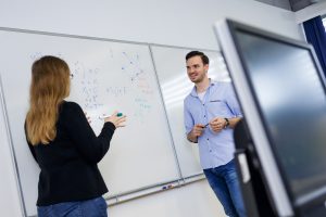 Lehrende arbeitet mit Studierendem am Whiteboard