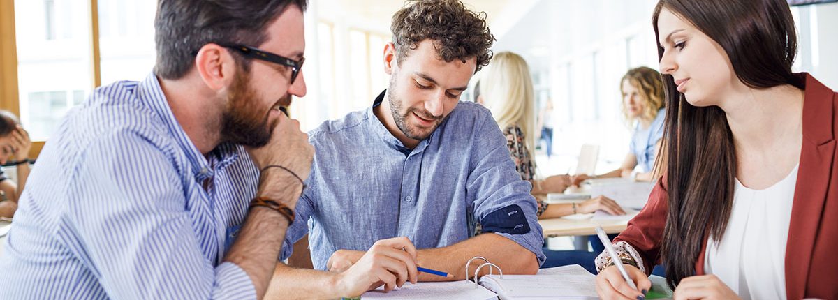 Drei Studierende an einem Tisch in der Aula