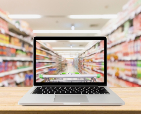 laptop computer on wood table with supermarket aisle blurred background online shopping concept