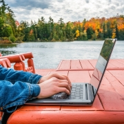 Jemand sitzt auf einer roten Sitzgarnitur an einem See und tippt auf einem Laptop
