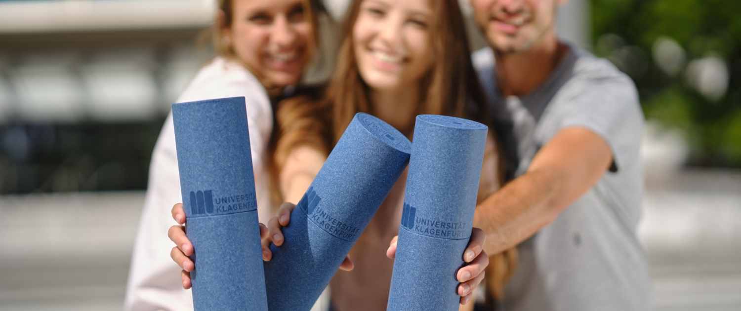 Dre Studierende halten drei Rollen mit Abschlussurkunden in die Kamararichtung
