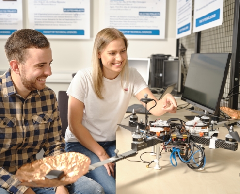 Zwei Studierende mit einer Drohne vor zwei PCs. Studentin zeigt auf die Drohne.