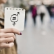 Nahaufnahme einer jungen Frauenhand, die ein Stück Papier mit einem Symbol für die Gleichstellung der Geschlechter in die Kamera zeigt.