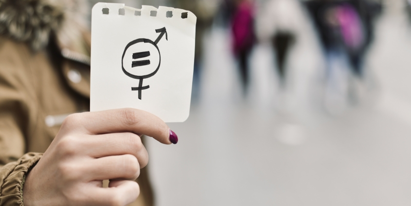 Nahaufnahme einer jungen Frauenhand, die ein Stück Papier mit einem Symbol für die Gleichstellung der Geschlechter in die Kamera zeigt.