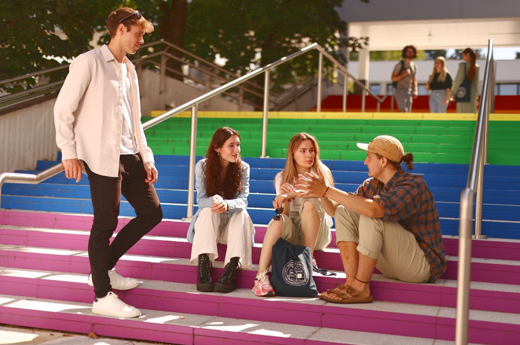 Studierendengruppe unterhält sich auf bunter Treppe auf dem Campus der Universität Klagenfurt.